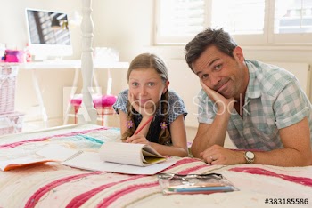 Portrait playful father helping daughter with homework on bed