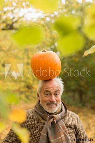 Portrait playful senior man with pumpkin on head in autumn park