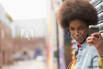 Portrait playful young woman with afro taking selfie on city street