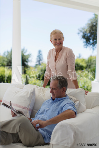 Portrait senior couple reading newspaper on patio sofa