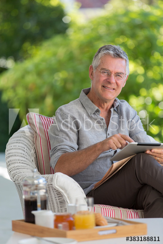 Portrait senior man enjoying breakfast and digital tablet on patio