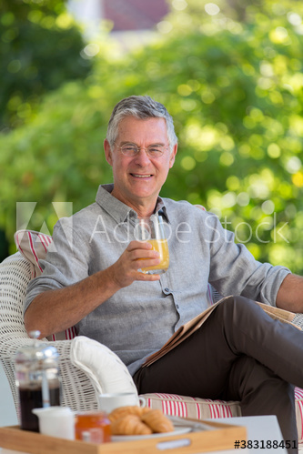 Portrait senior man with orange juice and newspaper on patio