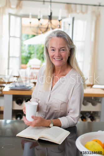 Portrait senior woman drinking tea and reading book in kitchen