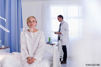 Portrait serious young female patient sitting on edge of hospital bed