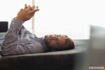 Portrait serious young man using smart phone on ottoman