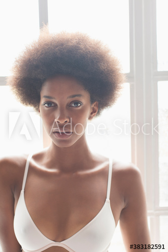 Portrait serious young woman with afro in bra at sunny window
