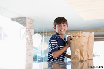 Portrait smiling boy unloading groceries in kitchen