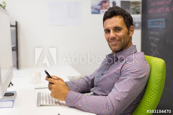 Portrait smiling businessman using smart phone at computer