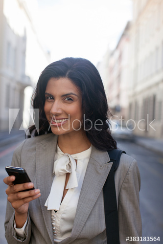 Portrait smiling businesswoman using smart phone on city street