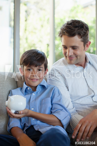 Portrait smiling father and son with piggybank on sofa