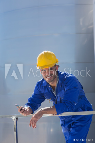 Portrait smiling male worker with smart phone in coveralls and hard hat