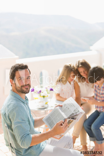 Portrait smiling man reading newspaper on sunny patio with family