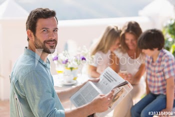 Portrait smiling man reading newspaper on sunny patio with family