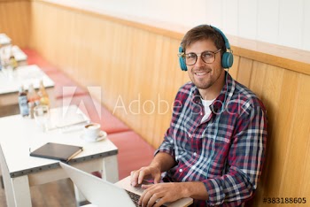 Portrait smiling man with headphones working at laptop in cafe