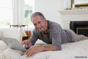 Portrait smiling senior man using laptop on ottoman