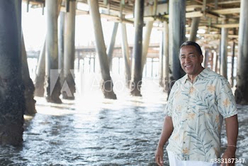 Portrait smiling senior man wading in ocean below pier