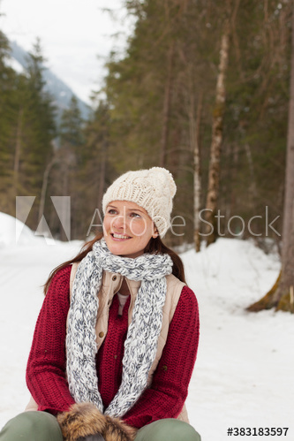 Portrait smiling woman in knit hat and scarf sitting in snowy woods