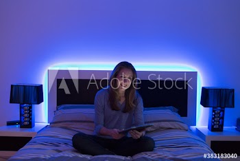 Portrait smiling woman using digital tablet on bed with neon headboard