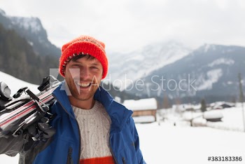 Portrait smiling young man carrying skis in snow