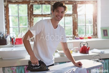 Portrait smiling young man ironing shirt in morning kitchen