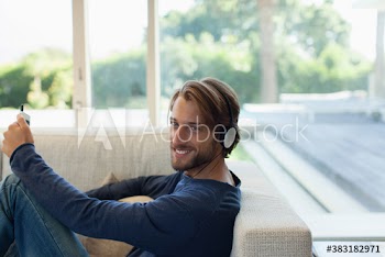 Portrait smiling young man listening to music with headphones on sofa