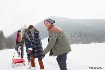 Portrait smiling young man sledding with friends in snowy field