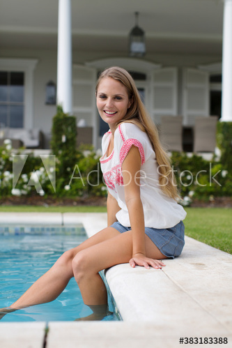 Portrait smiling young woman dipping legs in swimming pool