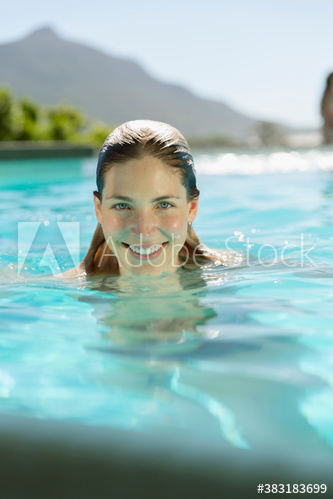Portrait smiling young woman swimming in sunny swimming pool