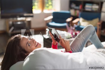 Portrait smiling young woman using digital tablet on sunny sofa