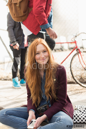 Portrait smiling young woman with smart phone on curb