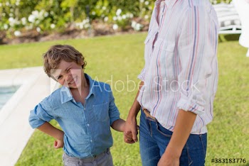 Portrait winking boy holding hands with mother in backyard