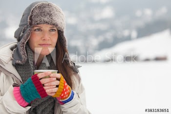 Portrait woman in fur hat drinking hot cocoa in snowy field