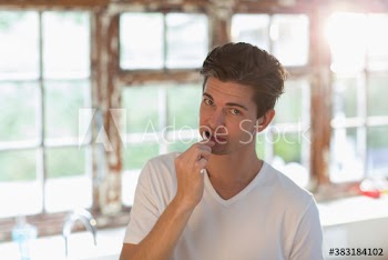 Portrait young man brushing teeth in sunny kitchen