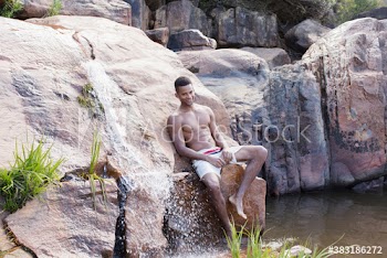 Portrait young man in swim trunks relaxing on rocks