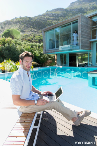 Portrait young man using laptop at sunny luxury poolside