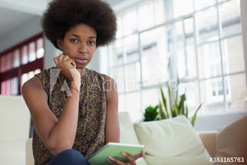 Portrait young woman with afro using digital tablet on sofa