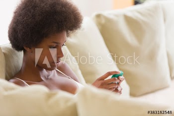 Portrait young woman with afro using smart phone on sofa