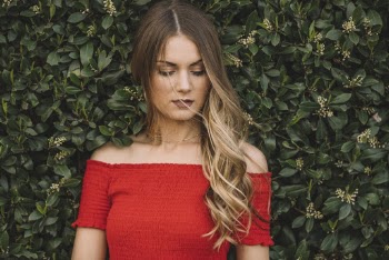 Potrait of Woman in Red Off-Shoulder Top Standing Infront of Green-Leafed Hedge