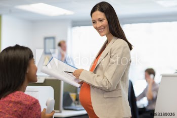 Pregnant businesswoman discussing paperwork with colleague in office