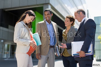 Pregnant businesswoman talking with colleagues in sunny parking lot