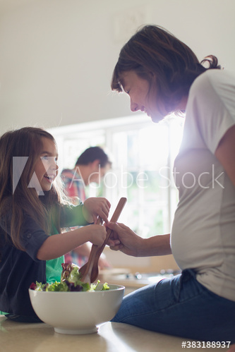 Pregnant mother and daughter preparing salad in kitchen