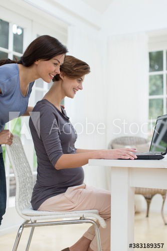 Pregnant woman and friend using laptop