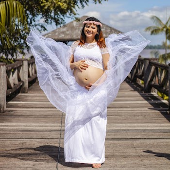 Pregnant Woman Standing at Wooden Dock Wearing White Crop Dress and Floral Tiara