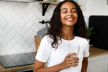 Pretty afro girl holds a glass of water and has happy look Free Photo