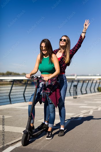 Pretty young female friends riding an electric scooter in the street