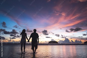 Rear view of adult tourist asian love couple holding hand on the beach with sunset sky background