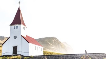 red and white concrete church near gray mountains under cloudy sky