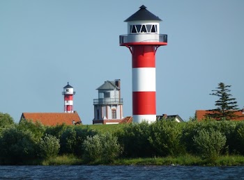 Red and White Striped Lighthouse Surrounded With Trees Near Body of Water