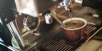 red ceramic mug filled with brown coffee near black and gray coffeemaker