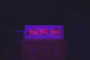 Red neon "Hurt Me" sign on top of a crate with arrow stickers